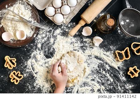 Woman's hands knead dough on table with flour, eggs and ingredients. Top view. Woman's hands knead dough on table with flour, eggs and ingredients. Top view. 91411142