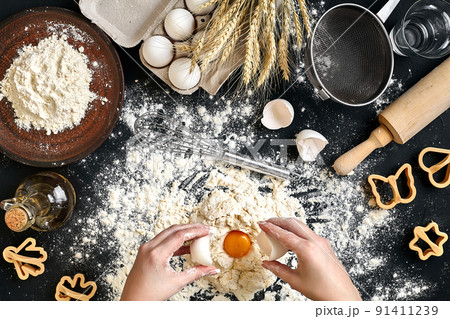 Woman smashes an egg using knife while kneading a pastry. Studio shot. Top view Woman smashes an egg using knife while kneading a pastry. Studio shot. Top view 91411239