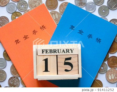散らばった日本の硬貨を背景に重なった橙色と青色の年金手帳と2月の年金支給日を表した木製カレンダー 散らばった日本の硬貨を背景に重なった橙色と青色の年金手帳と2月の年金支給日を表した木製カレンダー 91411252