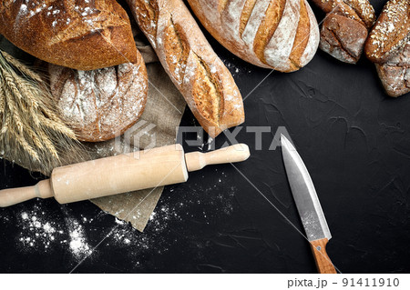 Top view of baguette, baked bread, flour and wheat spikes composition with wheat flour sprinkled around on a dark background Top view of baguette, baked bread, flour and wheat spikes composition with wheat flour sprinkled around on a dark background 91411910