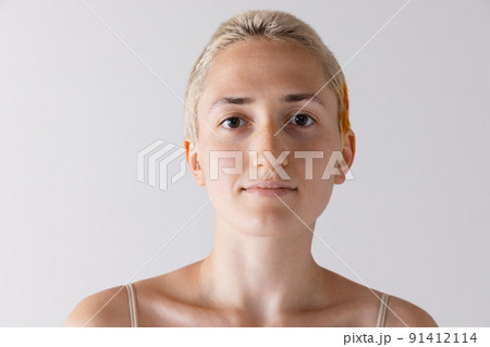 Portrait of young short-haired blonde girl posing, looking at camera isolated over grey studio background. Calmness Portrait of young short-haired blonde girl posing, looking at camera isolated over grey studio background. Calmness 91412114
