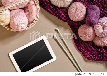 Pink and purple balls of wool threads with knitting needles lying in basket on beige background. Mock up background for your craft knitting Pink and purple balls of wool threads with knitting needles lying in basket on beige background. Mock up background for your craft knitting 91413044