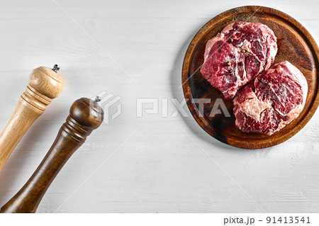 Raw beef steak with spices and ingredients for cooking on wooden cutting board and white background. 91413541