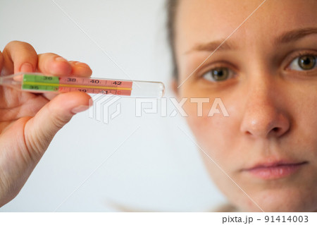 Woman being sick having flu looking at temperature on thermometer. 91414003