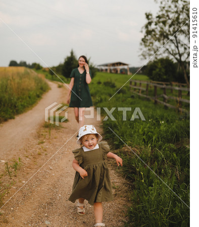 Happy family, active mother with little child, adorable toddler girl. Happy mom is playing with a toddler girl outdoors in summer Happy family, active mother with little child, adorable toddler girl. Happy mom is playing with a toddler girl outdoors in summer 91415610