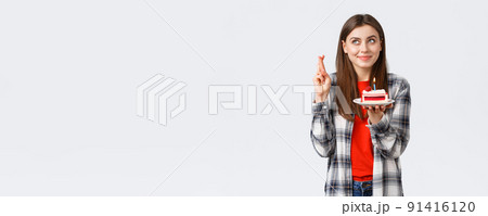 People lifestyle, holidays and celebration, emotions concept. Dreamy hopeful birthday girl in casual clothes, cross fingers and look up making wish, holding b-day cake, blowing candle 91416120