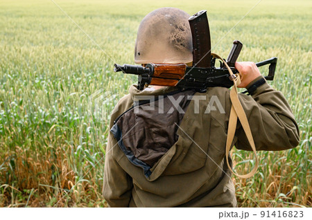 A soldier with a machine gun stands in a field, Ukrainian wheat fields and war. A soldier with a machine gun stands in a field, Ukrainian wheat fields and war. 91416823