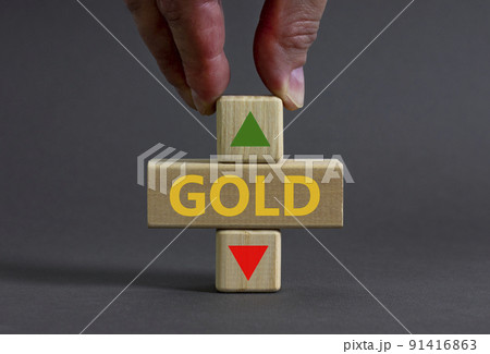 Gold price symbol. Businessman holds a wooden cube with arrow symbolizing that Gold price are going down or up. Beautiful grey table grey background. Business and gold price concept. Copy space. 91416863