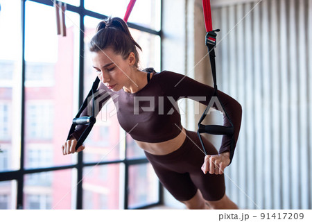 Fit woman doing push-up exercise with trx 91417209