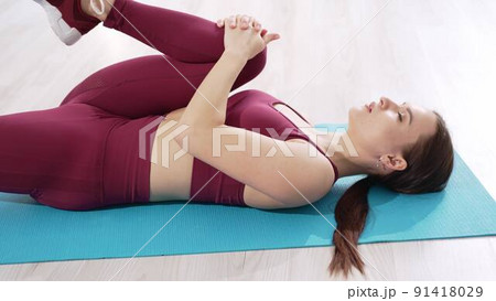 a beautiful and athletic girl in a burgundy tracksuit does exercises for stretching muscles a beautiful and athletic girl in a burgundy tracksuit does exercises for stretching muscles 91418029