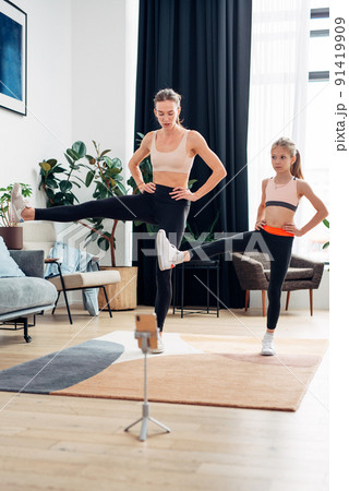 Home training. Mother and daughter warming up, stretching leg muscles Home training. Mother and daughter warming up, stretching leg muscles 91419909