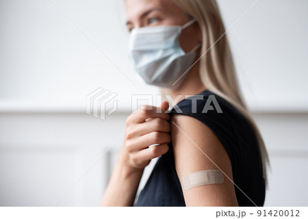 Woman showing her arm with bandage after receiving vaccination 91420012