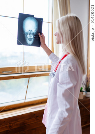 Woman doctor at window looking at skull scan Woman doctor at window looking at skull scan 91420021
