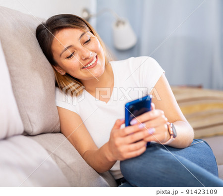 Latino woman with a mobile phone on the sofa at home Latino woman with a mobile phone on the sofa at home 91423109
