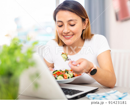 Housewife watching movie on laptop and eating vegetable salad Housewife watching movie on laptop and eating vegetable salad 91423181
