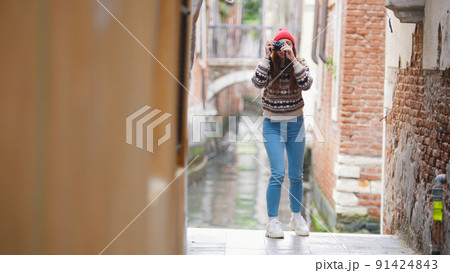 A young woman standing near the water channel and taking a photo on her camera - Venice, Italy 91424843