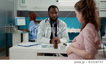 Male obstetrician having checkup appointment with pregnant patient, talking about maternity and childbirth in medical cabinet. Health specialist consulting woman with pregnancy belly. Male obstetrician having checkup appointment with pregnant patient, talking about maternity and childbirth in medical cabinet. Health specialist consulting woman with pregnancy belly. 91428747