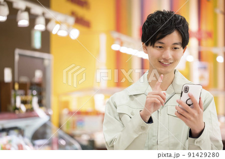 スーパーでスマホをチェックする作業服姿の若い男性 91429280