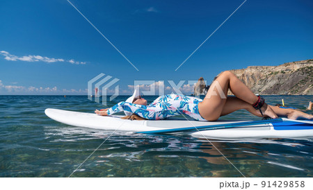 Healthy happy fit woman in bikini relaxing on a sup surfboard, floating on the clear turquoise sea water. Recreational Sports. Stand Up Paddle boarding. Summer fun, holidays travel. Active lifestyle Healthy happy fit woman in bikini relaxing on a sup surfboard, floating on the clear turquoise sea water. Recreational Sports. Stand Up Paddle boarding. Summer fun, holidays travel. Active lifestyle 91429858