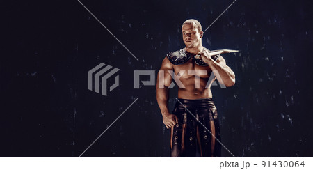 Studio shot of muscular ancient warrior man posing with axe Studio shot of muscular ancient warrior man posing with axe 91430064