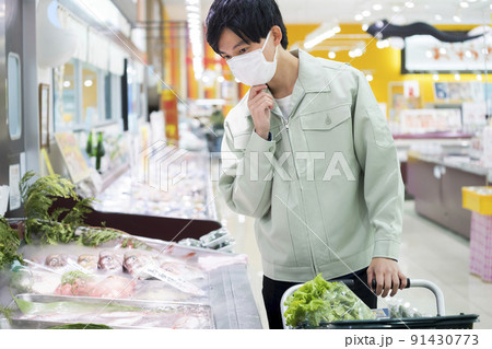 スーパーの鮮魚売り場で買い物をするマスク姿の作業服男性 91430773