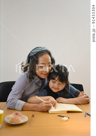Smiling middle aged grandma and little preschooler granddaughter drawing together at home Smiling middle aged grandma and little preschooler granddaughter drawing together at home 91433304