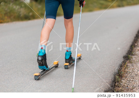 Legs of a biathlete athlete with ski poles, close-up. Concept of rollers ski and summer workout Legs of a biathlete athlete with ski poles, close-up. Concept of rollers ski and summer workout 91435953
