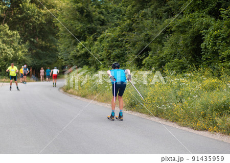 Roller ski olympiad. Group of athletes training before the competition. View from the back. Biathlon ride on the roller skis with ski poles, in the helmet. Concept of sport and summer contest Roller ski olympiad. Group of athletes training before the competition. View from the back. Biathlon ride on the roller skis with ski poles, in the helmet. Concept of sport and summer contest 91435959