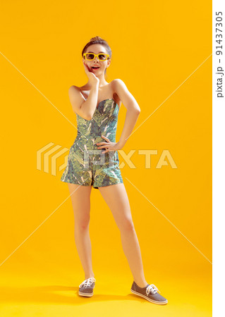 Full-length portrait of beautiful young girl posing isolated over yellow studio background. Emotive 91437305