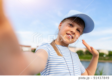 Portrait of little cute beautiful blond caucasian girl wear blue cap enjoy having fun taking selfie photo phone camera resting at beach outdoors on summer day. Children blogging and video streaming Portrait of little cute beautiful blond caucasian girl wear blue cap enjoy having fun taking selfie photo phone camera resting at beach outdoors on summer day. Children blogging and video streaming 91437849