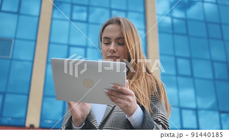 A young girl student works with a white tablet in the city. 91440185