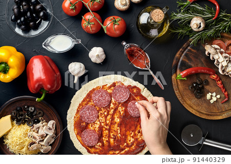 Hands of baker adding ingredients into pizza during pizza preparation at kitchen 91440329