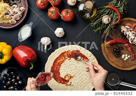 Hands of baker adding ingredients into pizza during pizza preparation at kitchen 91440332