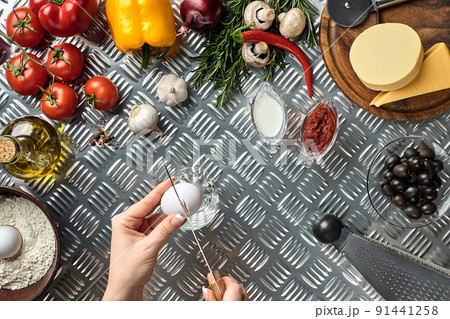 Set of ingredients for pizza and baker's hand smash eggs on metal table 91441258
