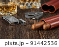 Two Cuban cigars, a cutter and a lighter in a leather case on an old brown table 91442536