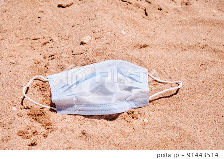 Blue medical mask lies on the sand on the beach Blue medical mask lies on the sand on the beach 91443514