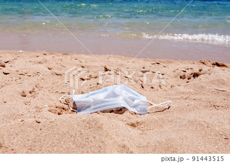 Medical mask lies on the sand on the beach, sea background. removal of used medical face mask. Beach day during covid-19 coronavirus pandemic Medical mask lies on the sand on the beach, sea background. removal of used medical face mask. Beach day during covid-19 coronavirus pandemic 91443515