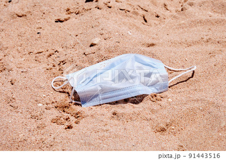 Medical mask on the sand of the beach as a reminder of the pandemic Medical mask on the sand of the beach as a reminder of the pandemic 91443516