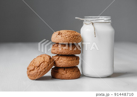 Milk in a glass jar and oatmeal cookies on a white table background. Copy, empty space for text 91448710