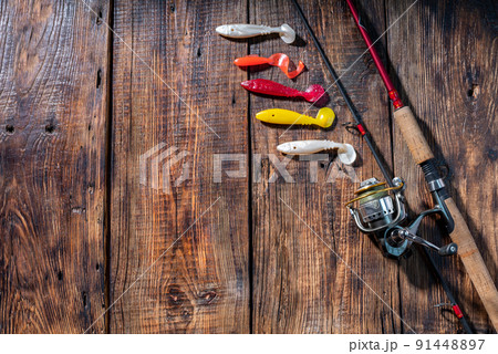 Spinning reel and soft silicone lures. Fishing composition on a wooden board. Lures in the form of fish. Spinning reel and soft silicone lures. Fishing composition on a wooden board. Lures in the form of fish. 91448897