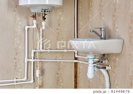 Plumbing pipeline of home water supply with electric water heater tank and sink in country house. 91449679