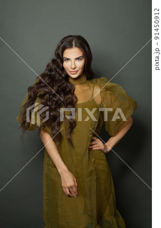 Brunette model woman with long dark wavy hairstyle in green dress standing on black background Brunette model woman with long dark wavy hairstyle in green dress standing on black background 91450912