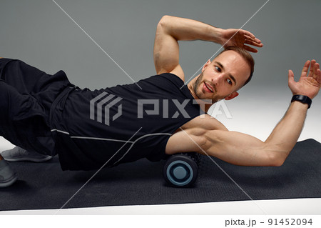 Athletic man using a foam roller to relieve sore muscles after a workout. Athletic man using a foam roller to relieve sore muscles after a workout. 91452094