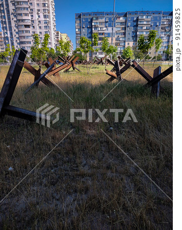Iron anti-tank structures on the background of city buildings. Iron anti-tank structures on the background of city buildings. 91459825