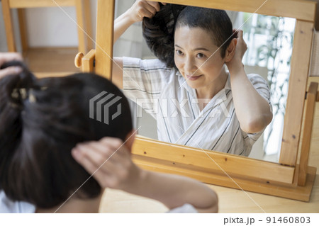 鏡に向かってウイッグをつけるミドルの女性　がん患者アピアランスケア　イメージ 91460803