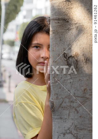 Female child peeks out from behind a tree. Female child peeks out from behind a tree. 91461262