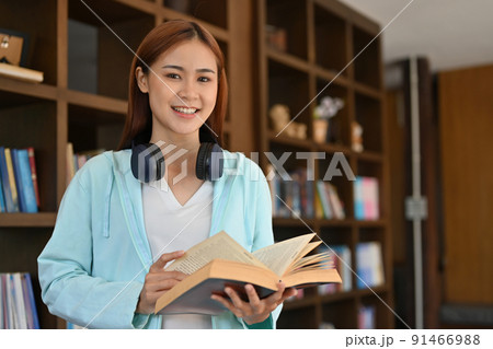Attractive young Asian female college student standing in the library with a book. Attractive young Asian female college student standing in the library with a book. 91466988