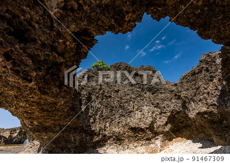 Beach cave in a rock formation, blue sky, green plant, cloud. 91467309