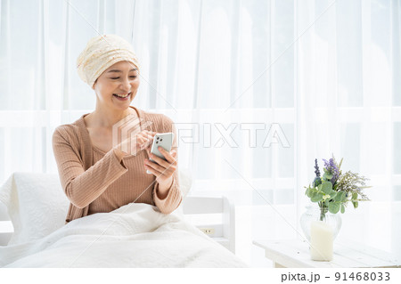 ベッドでスマホを見る医療用帽子をかぶったミドル女性 ベッドでスマホを見る医療用帽子をかぶったミドル女性 91468033