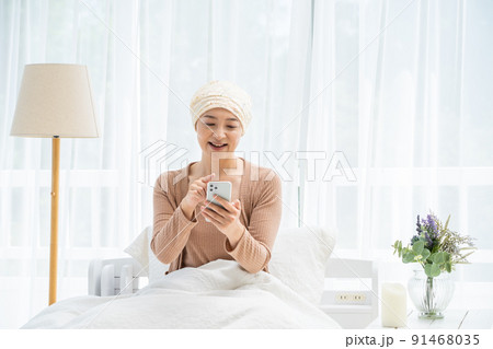 ベッドでスマホを見る医療用帽子をかぶったミドル女性 ベッドでスマホを見る医療用帽子をかぶったミドル女性 91468035